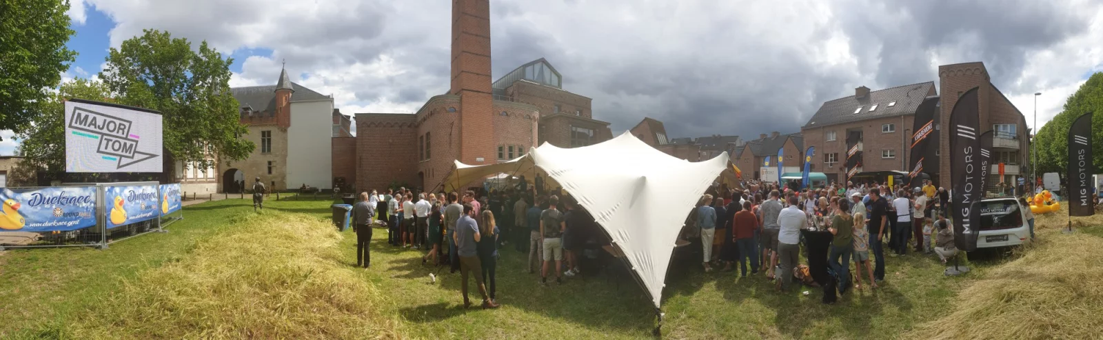Panorama van het Duck Race-dorp in Gent, met een grote tent, bezoekers en een scherm met het Major Tom-logo