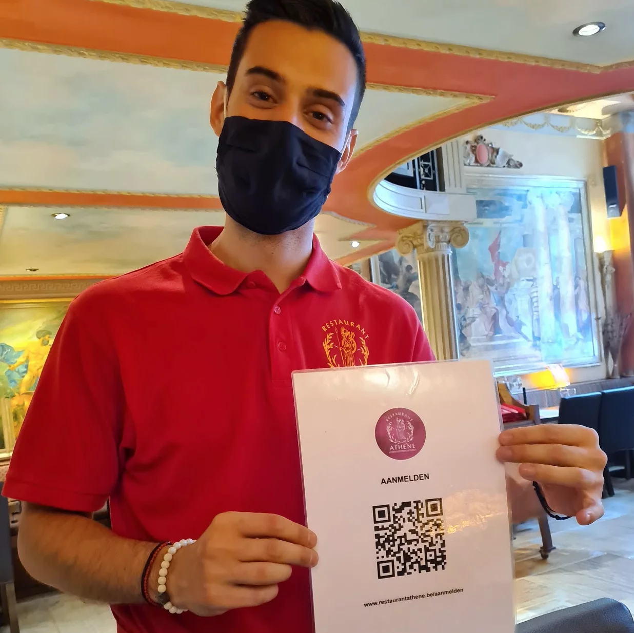 Een ober van restaurant Athene met mondmasker toont een kaartje met de QR-code om je aan te melden