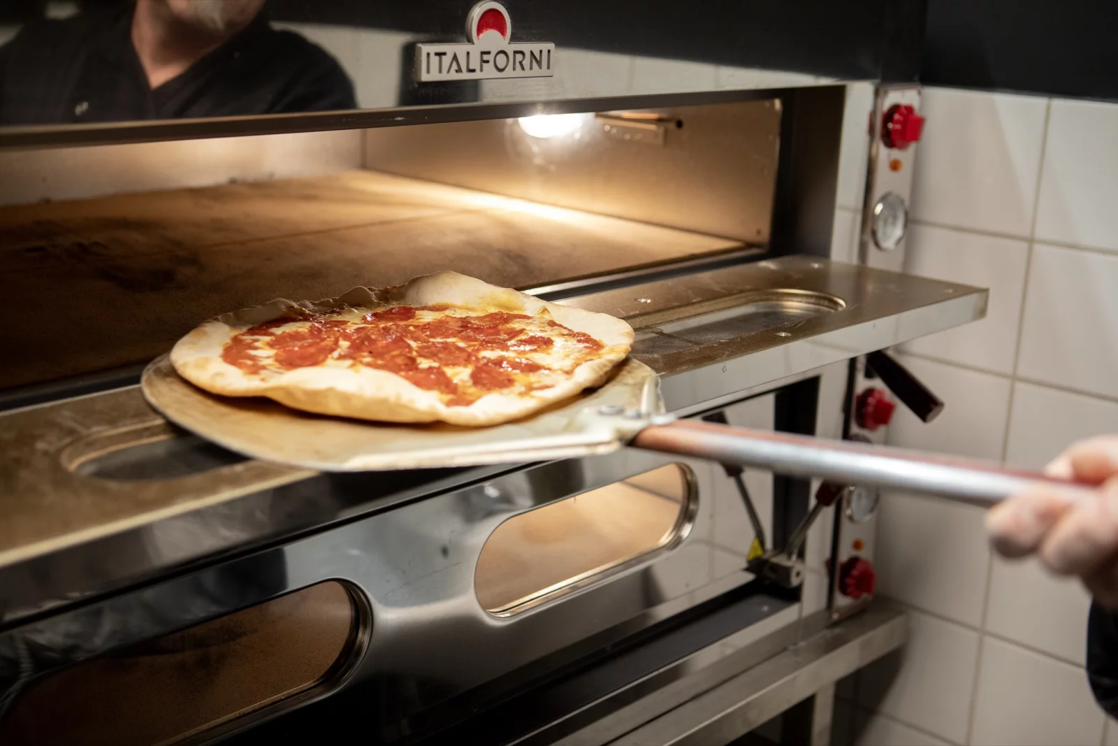 Een pizza gaat met een pizzaschep de oven in bij Il Padrino