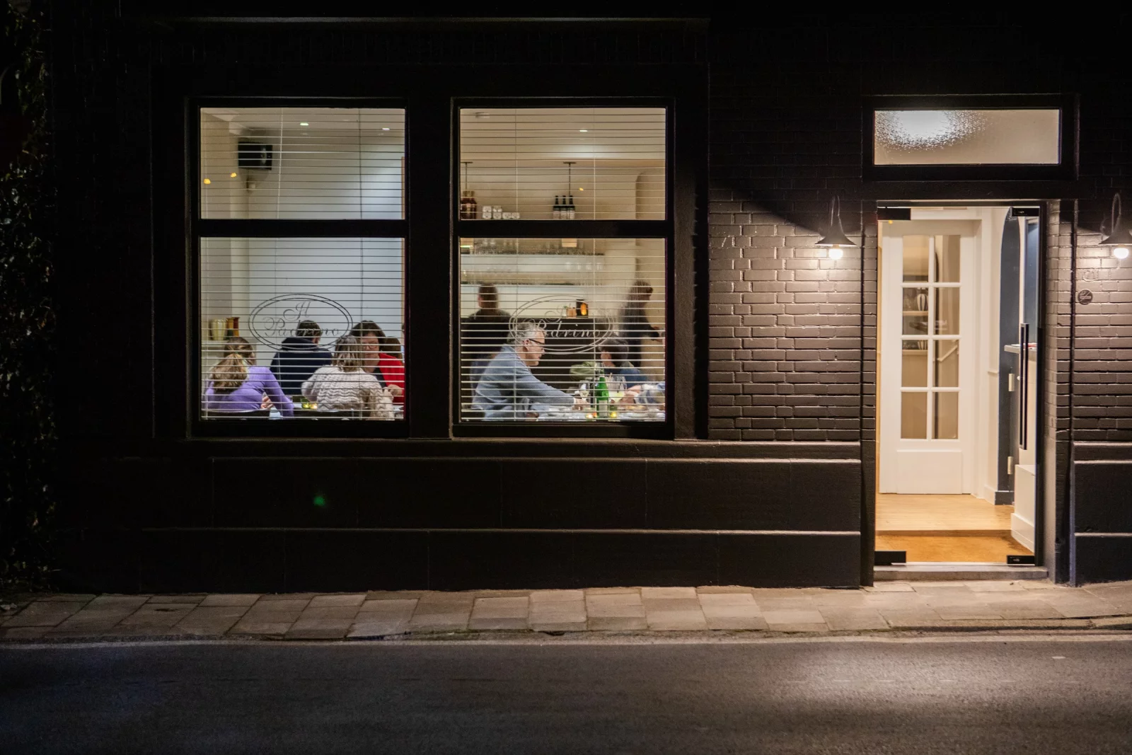 De gevel van Il Padrino in Lovendegem bij avond, met de ramen verlicht