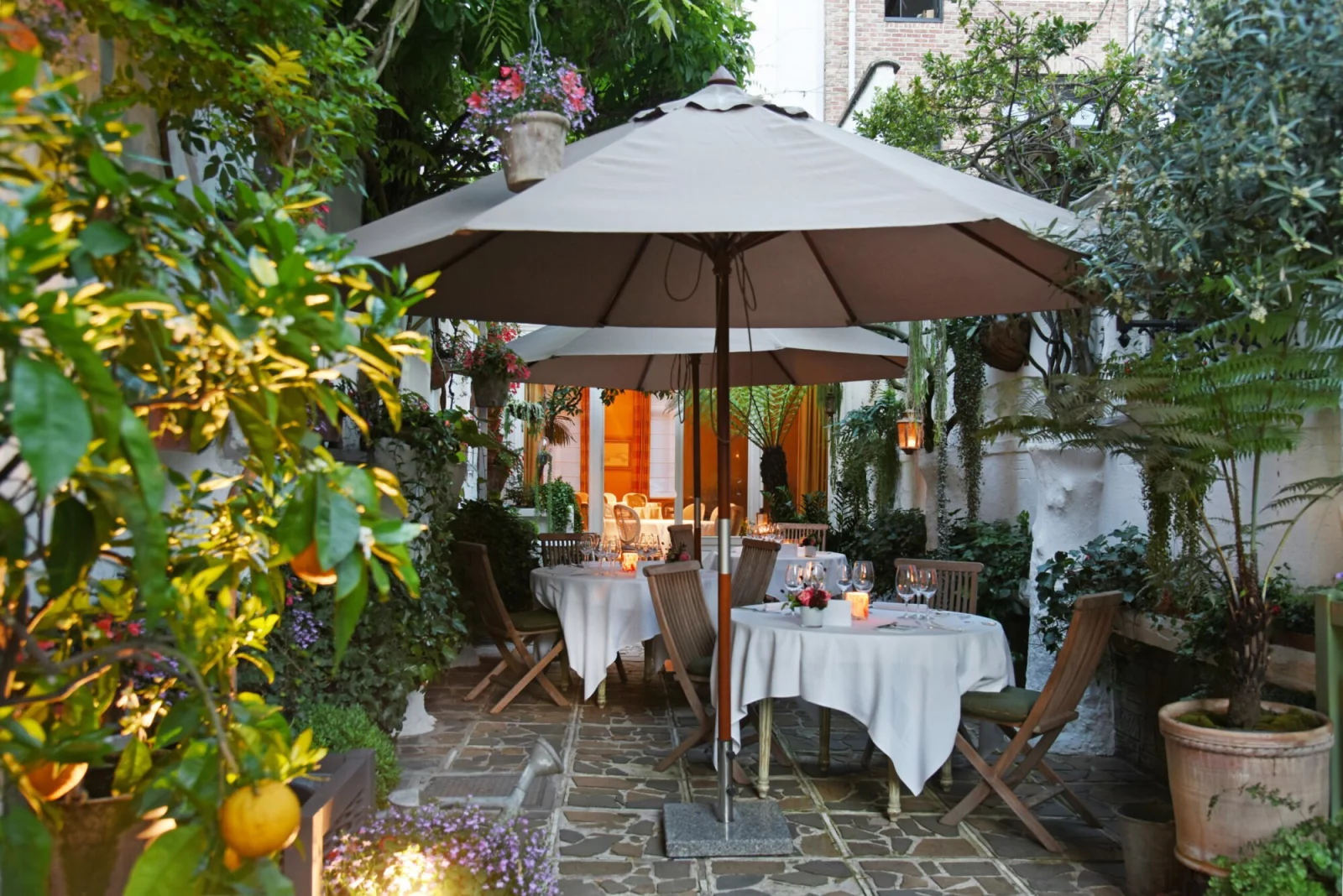 The garden terrace of restaurant Jan Van den Bon in evening light, with laid tables under a parasol