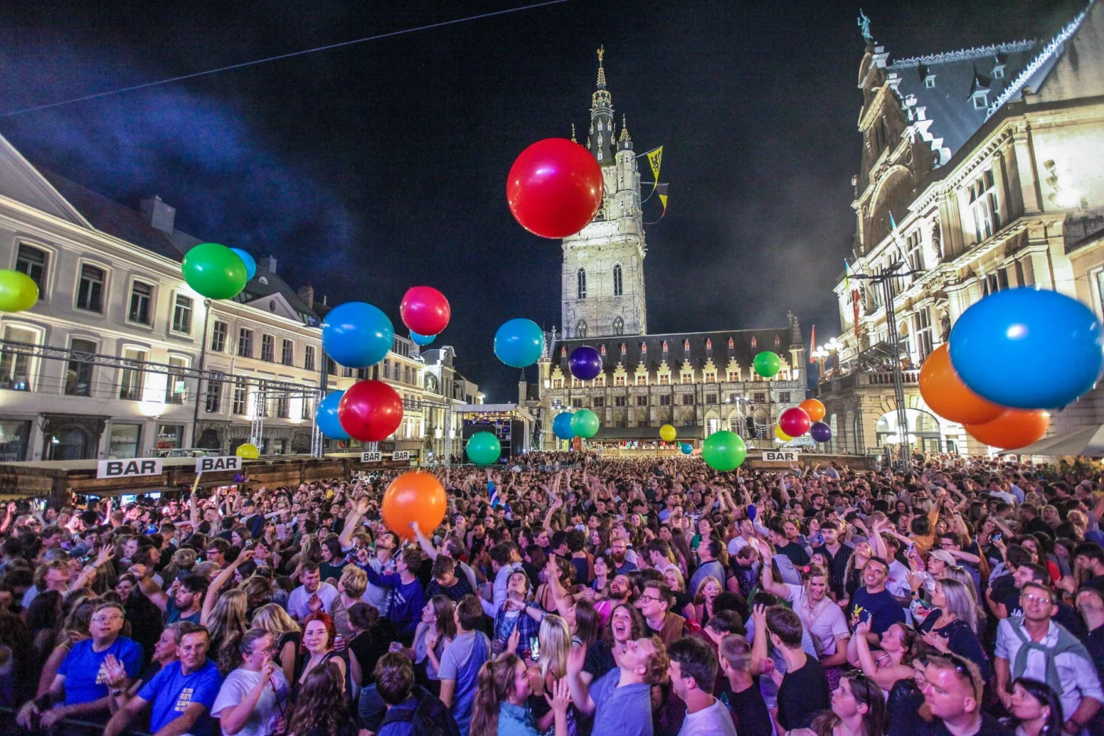 Sint-Baafsplein packed with festival-goers and big colourful balloons, with the Belfry in the background