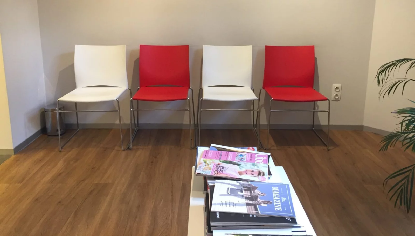 The waiting room at Huisartsen &rsquo;t Zuid: four white and red chairs against the wall, with a pile of magazines on the table in front of them