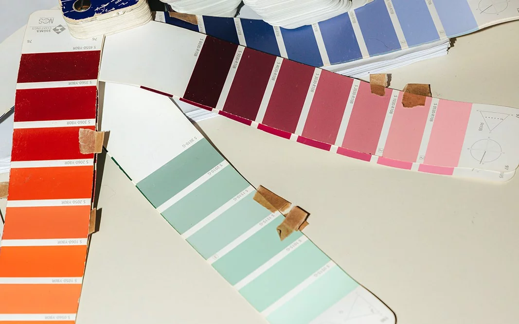 Kleurstalen in rood, oranje, bordeaux, roze, mintgroen en blauw op een tafel in de studio van Pi&egrave;ce Mont&eacute;e
