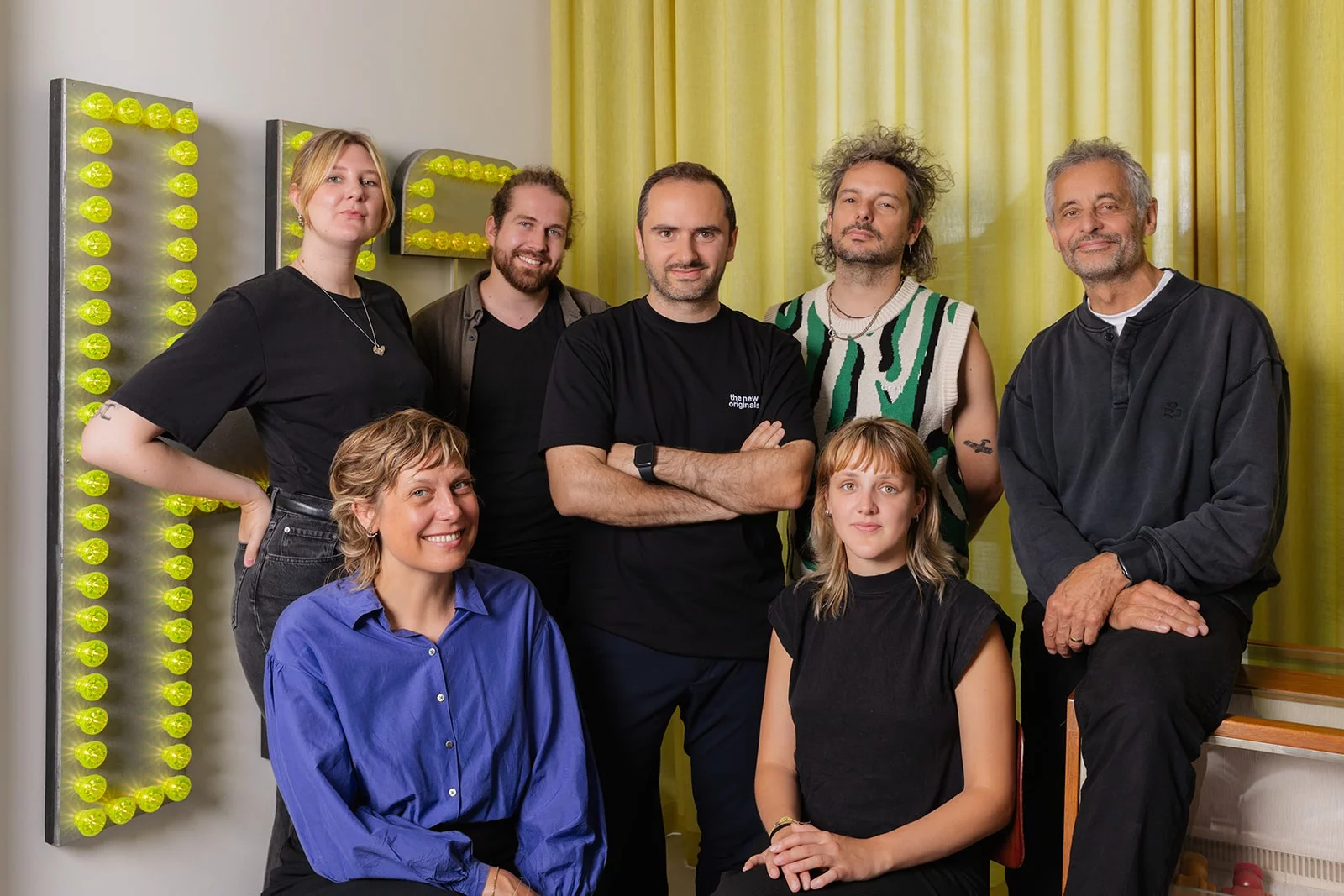 Het team van Pi&egrave;ce Mont&eacute;e in de studio, voor een wand met gele lichtletters