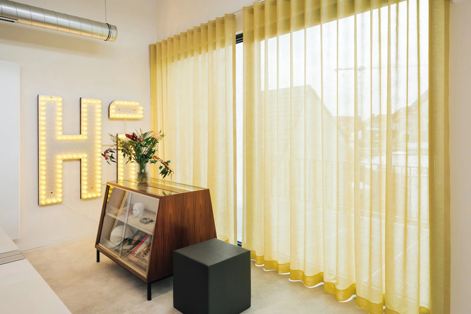 Het bureau van Pi&egrave;ce Mont&eacute;e in Gentbrugge met gele gordijnen, een vitrinekast en een grote lichtletter H