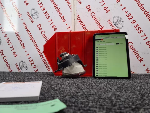 Een gedemonteerd Toyota-onderdeel voor een rode bak en een iPad met de onderdelenlijst, in de fotostudio van Toyota Parts De Coninck